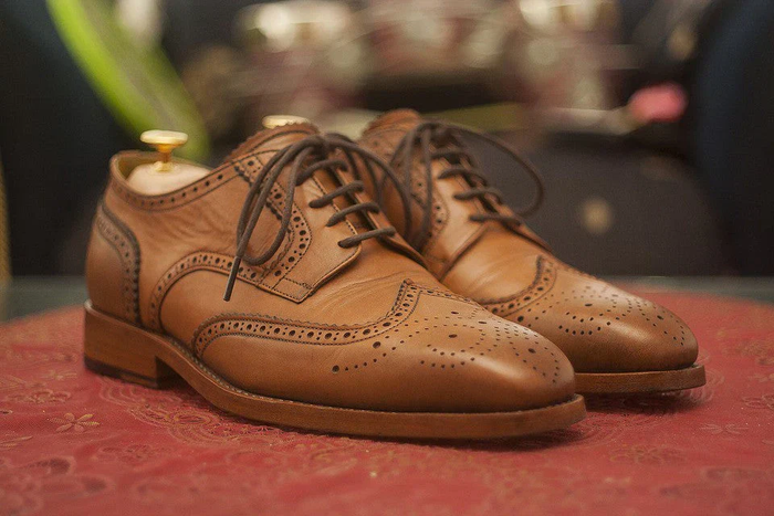 Pair of classic brown leather brogue shoes with detailed perforations, displayed on a patterned surface