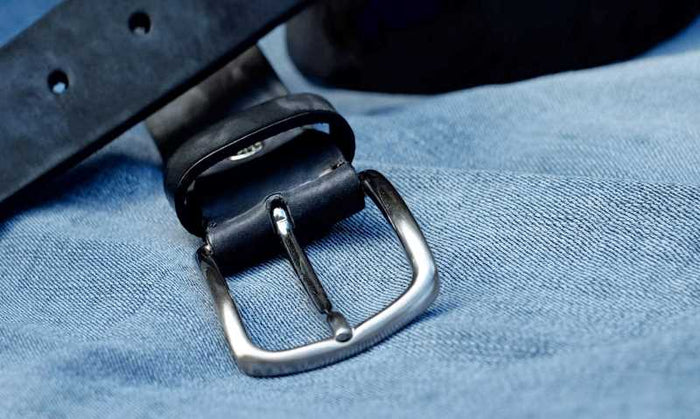 Close-up of a black leather belt with a silver buckle placed on blue denim fabric
