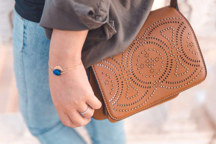 Close-up of a person carrying a tan leather handbag with decorative cut-out patterns and silver studs, styled with casual denim jeans and a dark top