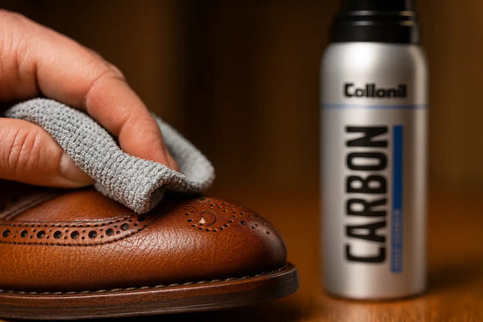 Close-up of a brown brogue being wiped with a microfiber cloth; Collonil Carbon Odor Cleaner can blurred in the background
